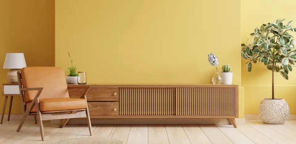 A yellow color wall in a living room with a wooden cabinet, chair and a flower vass